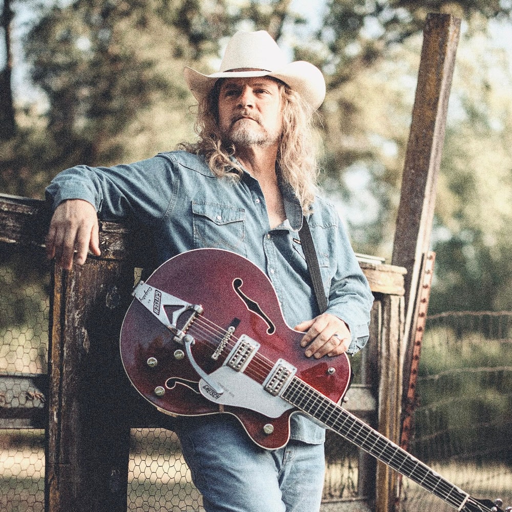Frank Hannon leaning on a fence with his Gretsch guitar
