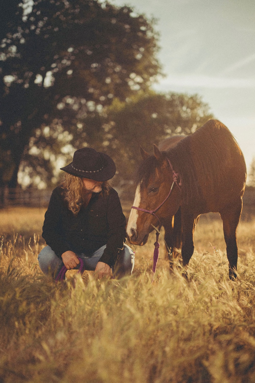 Frank Hannon kneeling beside a horse in a field