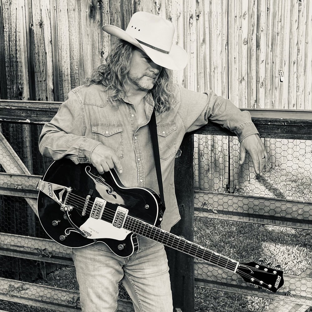 Frank Hannon with guitar at a wire fence, black and white