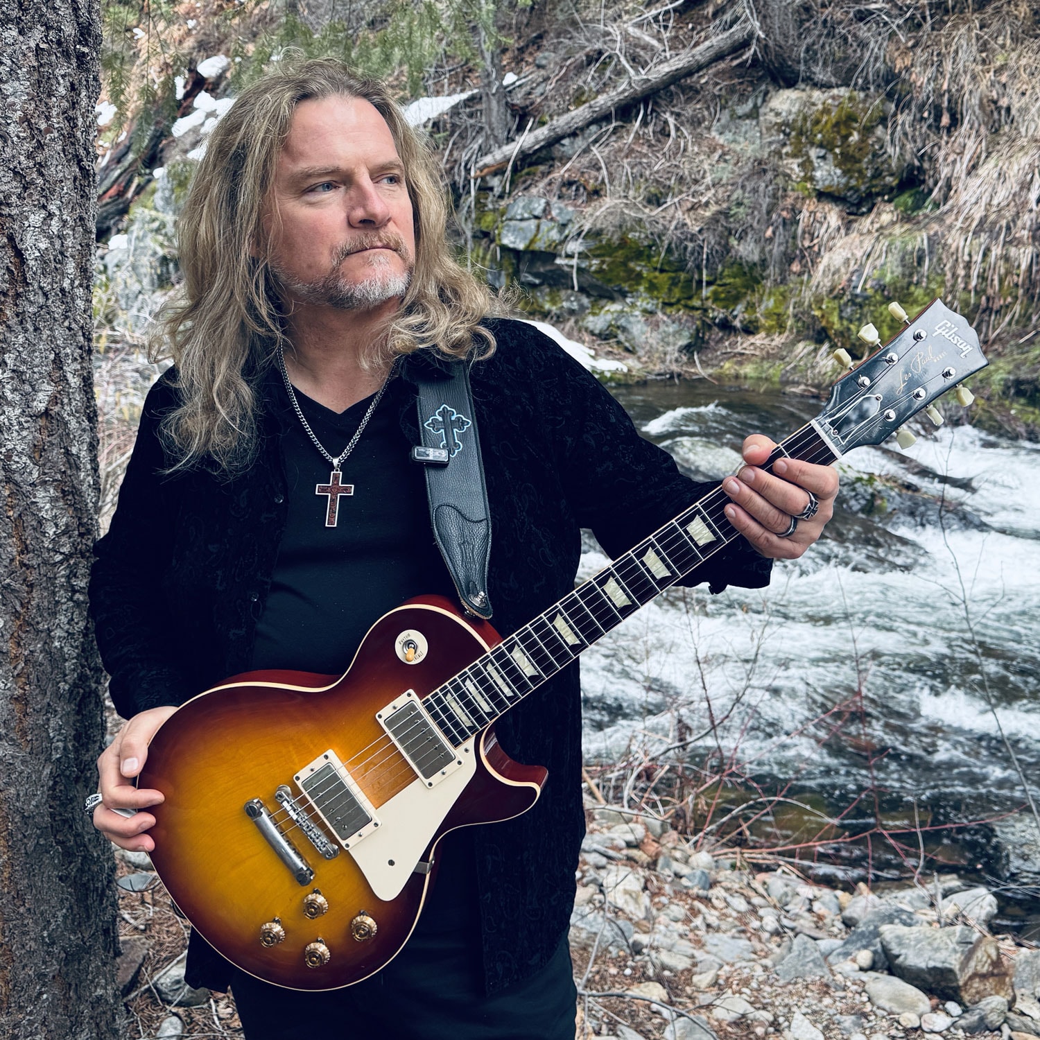 Frank Hannon holding a Gibson Les Paul by a mountain river